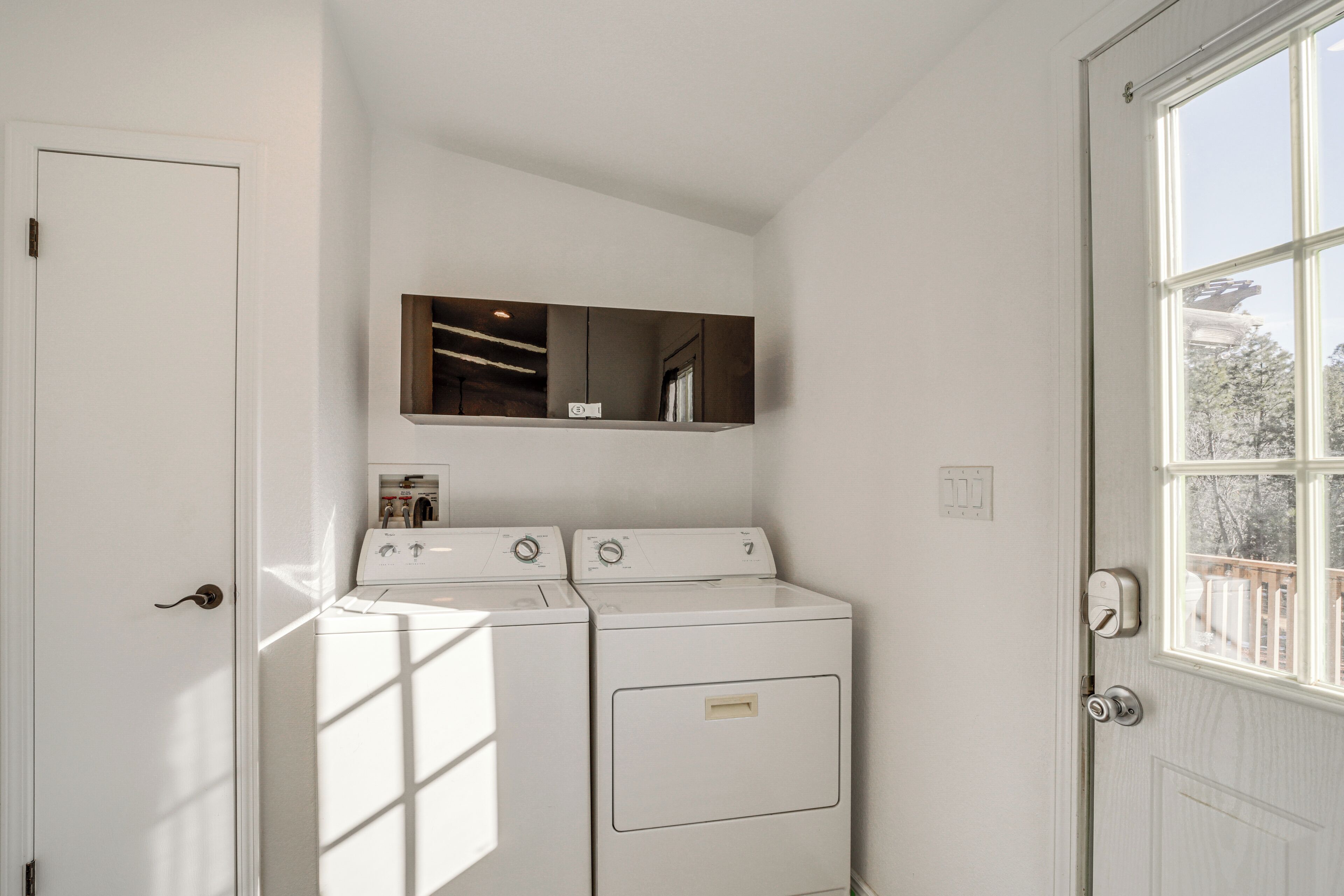 Une buanderie équipée de deux machines à laver et deux sèche-linge superposés, une étagère en bois au-dessus, et une porte avec une fenêtre sur le côté droit.