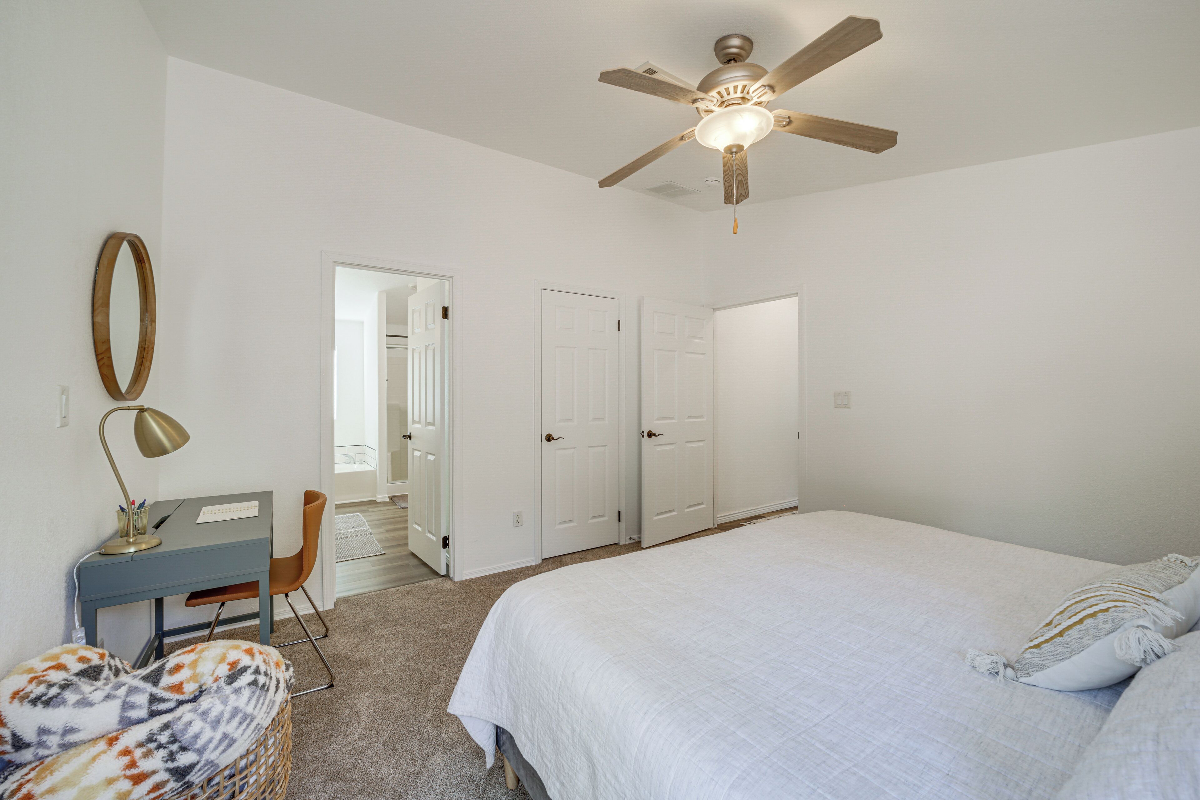A bedroom with a bed, a desk, a chair, a ceiling fan, and a wardrobe.