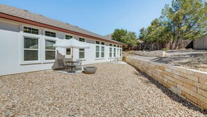 A modern house with a patio area featuring a table and chairs, a large planter, and a gravel driveway. - Idyllic Lago Vista Home < 1 Mi to Lake Travis! (Leander)