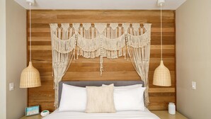 A bedroom with a wooden headboard, macrame wall hanging, two hanging lamps, a bed with white bedding, and a nightstand with a picture frame and a vase. - Mount Coolum Beachfront Abode with Private Rooftop (Coolum Region)