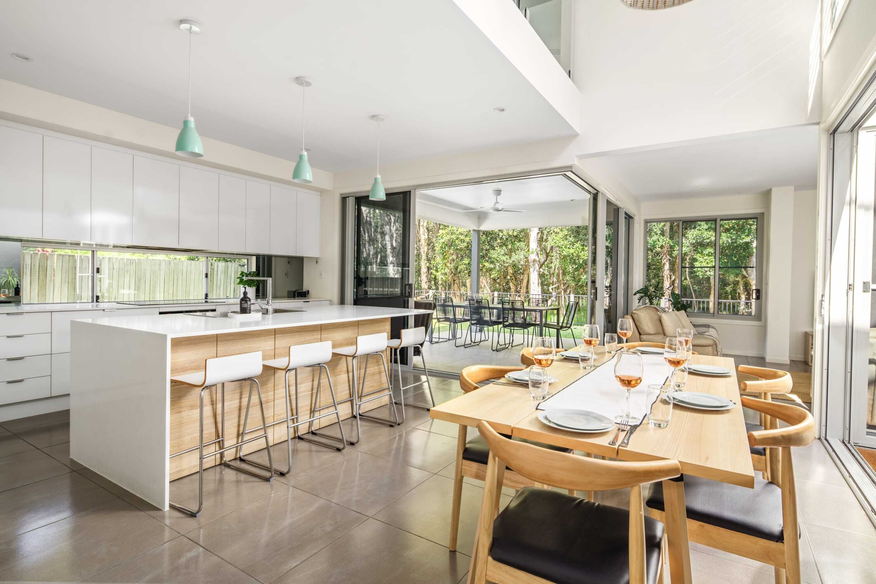 A modern kitchen with a central island, bar stools, and a dining area with a long table set for six.