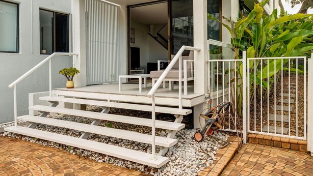 A modern two-story house with a balcony, a staircase, and a garden area.