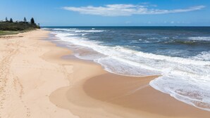 A beach with clear skies, waves, and a distant shoreline.