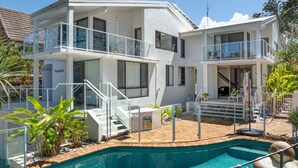 A modern two-story house with a swimming pool, outdoor seating, and a staircase leading to the upper floor.