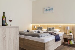 A modern bedroom with a wooden bed, bedside tables, a nightstand, and a wall-mounted lamp. - Pilger Apartments (Tihany)