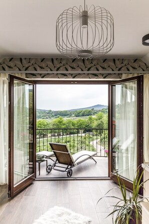 A room with a view of a balcony, a wicker chair, a small table, and a white furry rug. - Pilger Apartments (Tihany)