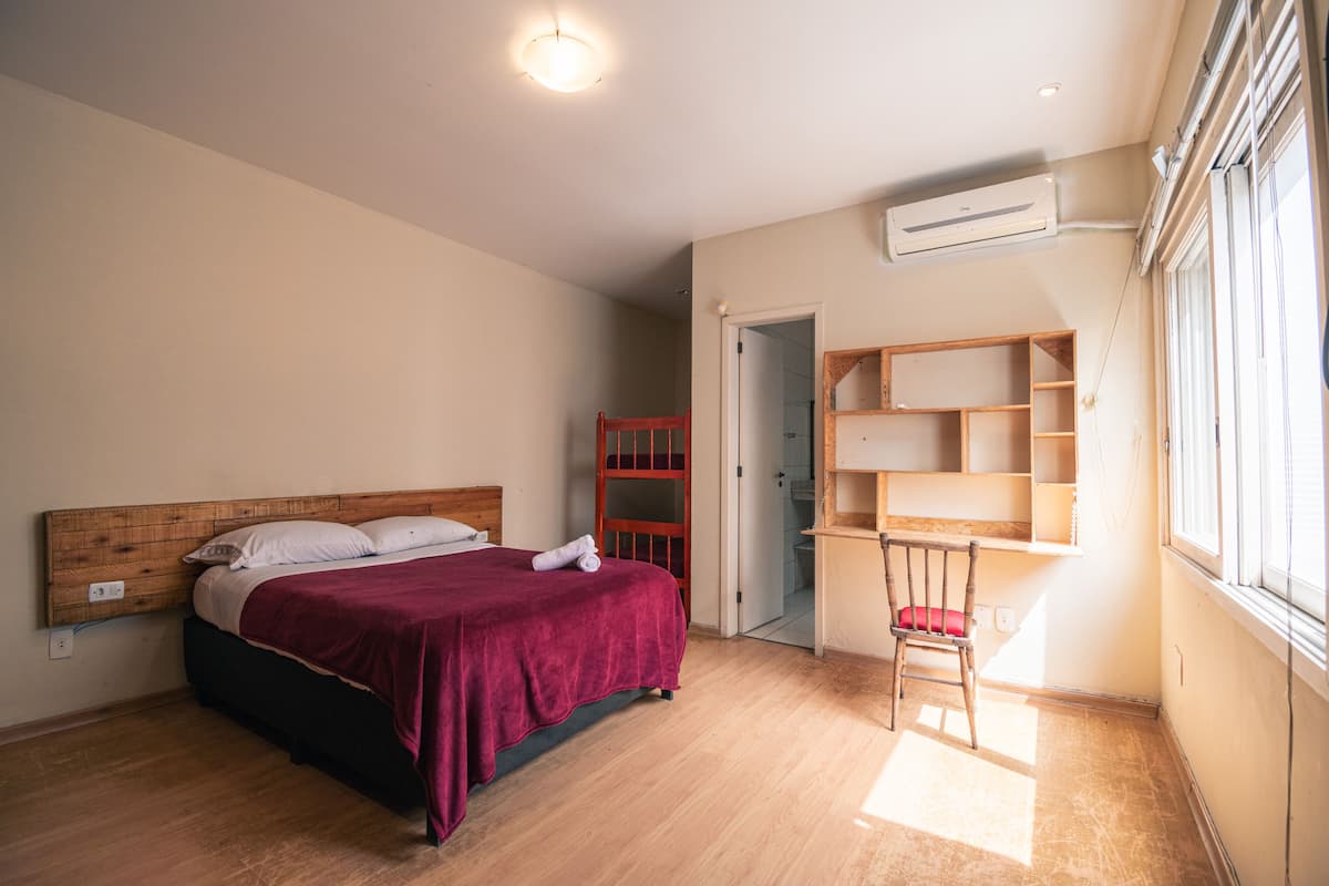 A bedroom with a bed, a chair, a desk, and a window.