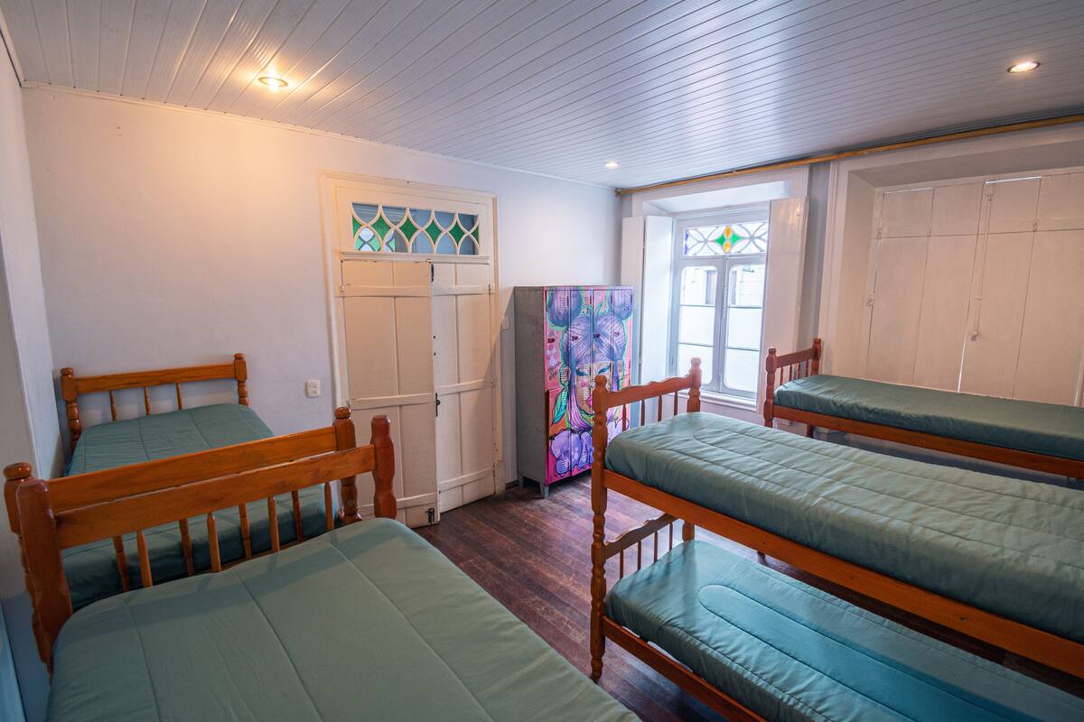 A room with four wooden bunk beds, a door with a stained glass window, and a colorful painting on the wall.