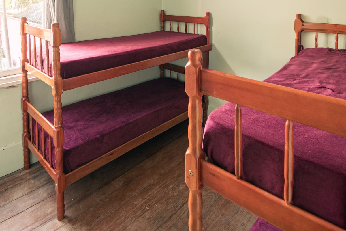 A room with two wooden bunk beds, a window with curtains, and a wooden floor.