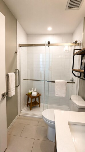 Un baño moderno con cabina de ducha de vidrio, inodoro y lavamanos con espejo superior.