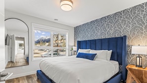 A bedroom with a large bed, a window with a mountain view, and a patterned wall.