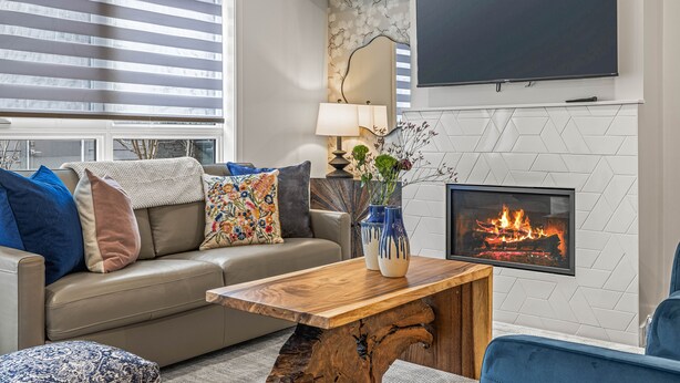 A modern living room with a sofa, a coffee table, a fireplace, and a flat-screen TV mounted on the wall.