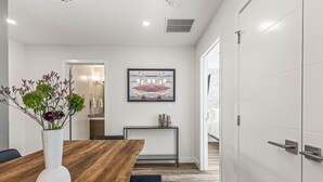 A modern dining area with a wooden table, a white vase with flowers, and a framed artwork on the wall.