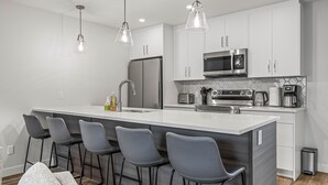 A modern kitchen with a large island, bar stools, stainless steel appliances, and pendant lighting.