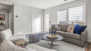 A modern living room with a grey sofa, round coffee table, and patterned ottomans.