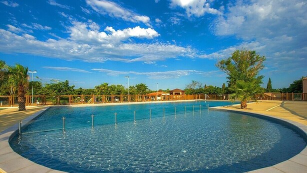 Une grande piscine circulaire Ă lâeau dâun bleu limpide, entourĂ©e dâune terrasse dallĂ©e et de palmiers.