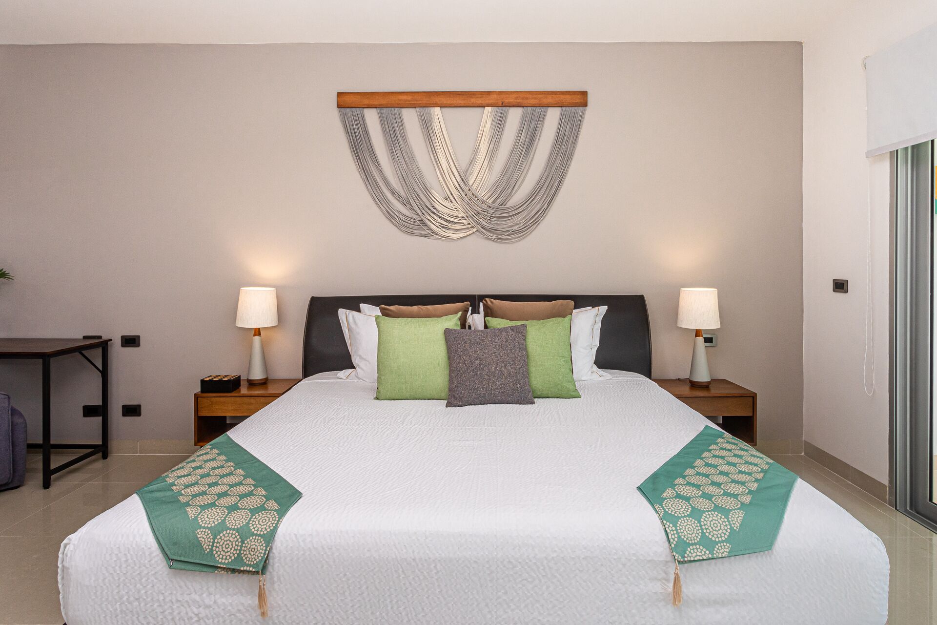 A neatly made bed with a white comforter and green decorative pillows, a wooden headboard, and two bedside lamps.