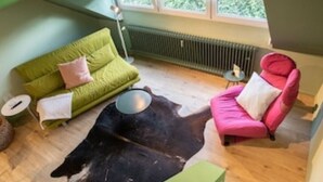 Ein Zimmer mit einem grünen Sofa, einem pinkfarbenen Sessel, einem schwarz-weißen Kuhfellteppich und einem kleinen runden Tisch.