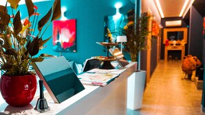 Ein Empfangsschalter mit einem Laptop, einer roten Vase mit Pflanzen und einem farbenfrohen, abstrakten Gemälde im Hintergrund.