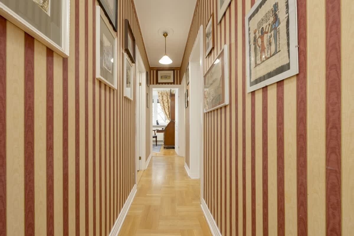 A hallway with striped wallpaper and framed pictures on the walls.