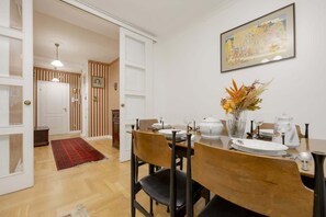 Un coin repas avec une table en bois dressée pour quatre personnes, un vase contenant des fleurs séchées et un tableau accroché au mur.