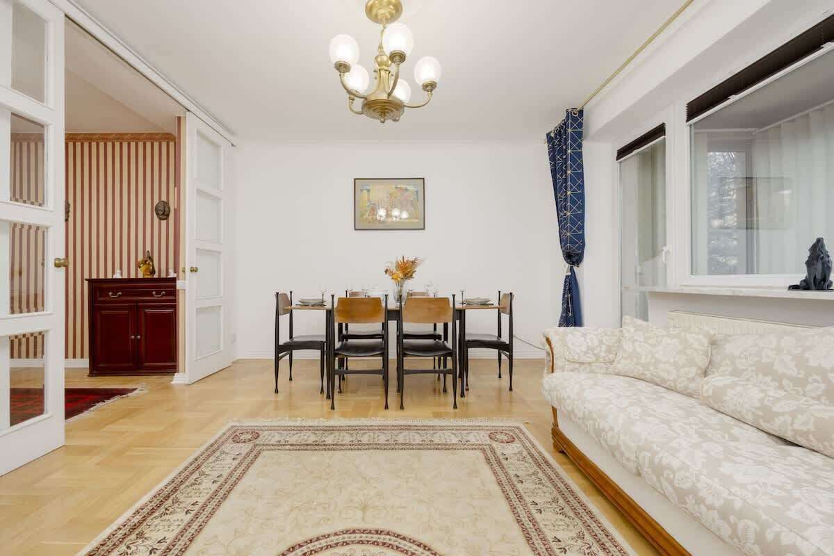 Uma sala de estar com área de jantar, um lustre, um sofá e uma janela com cortinas.
