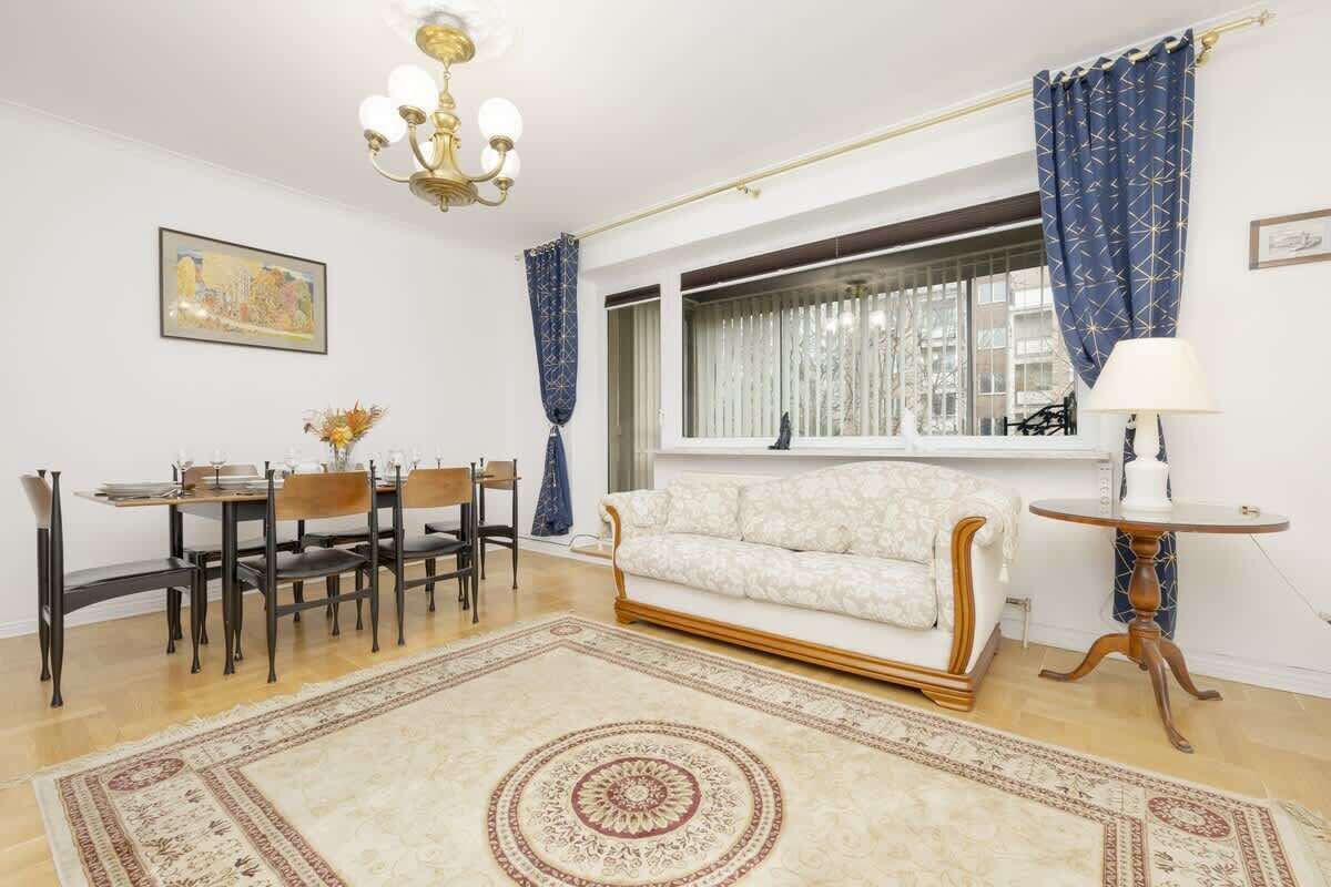 Una sala de estar con sofá, mesa de comedor, sillas, candelabro y ventana con cortinas.