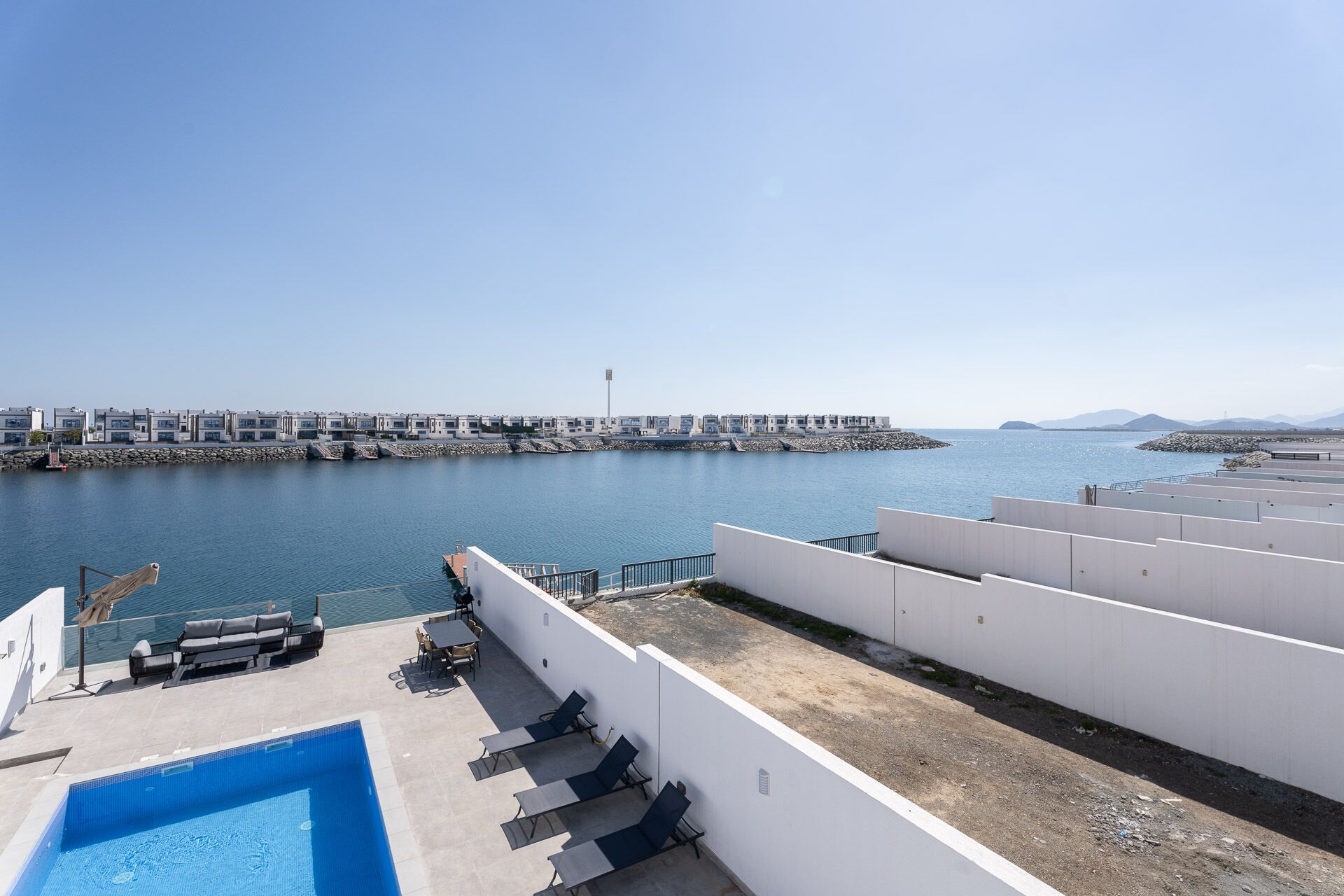 Un área de piscina en la azotea con vistas a un puerto deportivo y edificios al otro lado del agua.