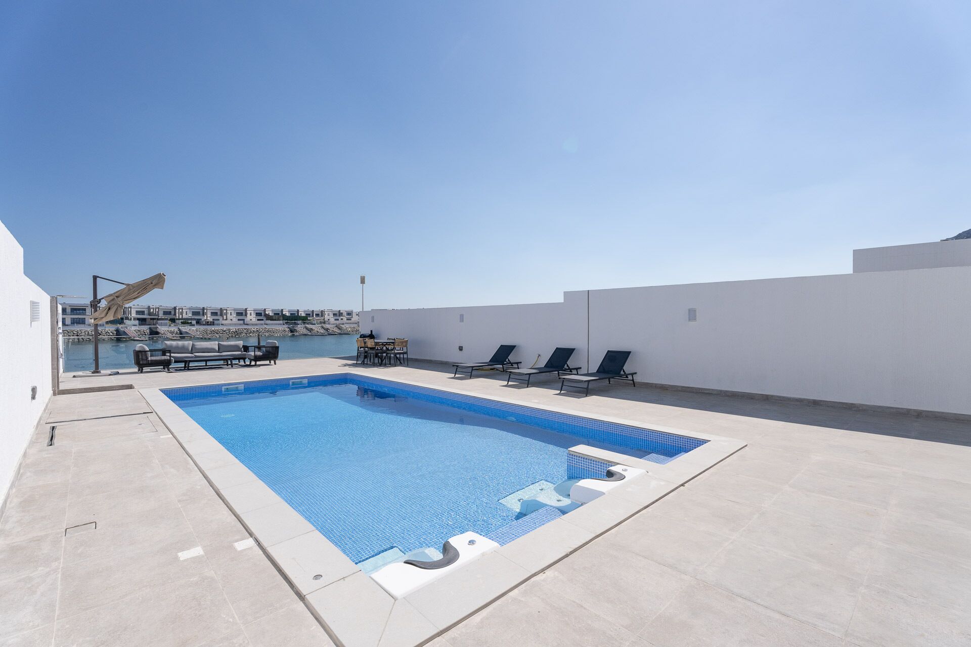 Ein Pool auf dem Dach mit freiem Blick auf das Meer, eine Lounge mit Sesseln und ein modernes Gebäude im Hintergrund.