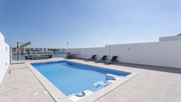 Ein Pool auf dem Dach mit freiem Blick auf das Meer, eine Lounge mit Sesseln und ein modernes Gebäude im Hintergrund.