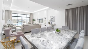 Uma sala de estar moderna com uma grande mesa de mármore, sofás cinza e vista para uma piscina.
