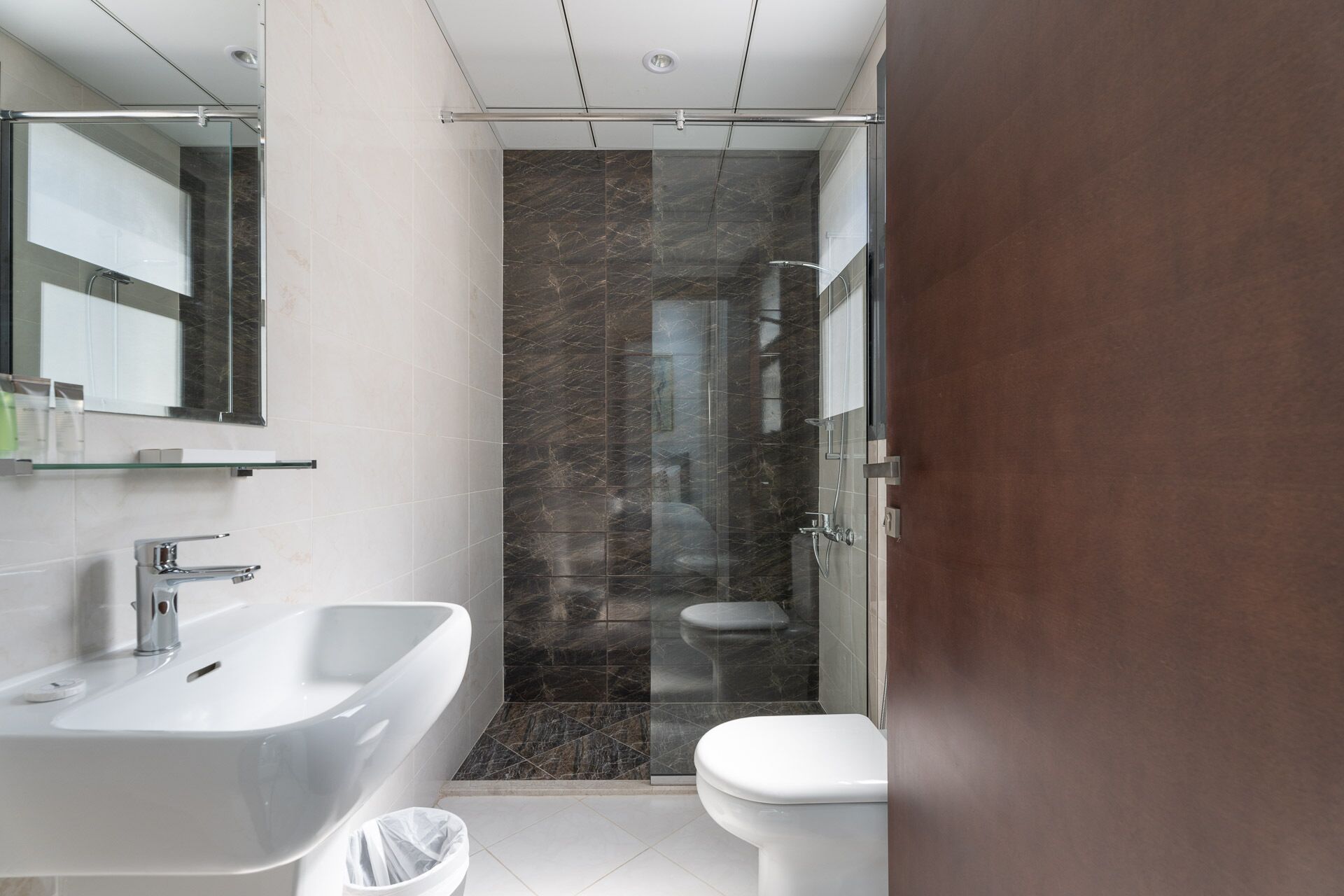 A modern bathroom with a white sink, a toilet, and a glass-enclosed shower area.