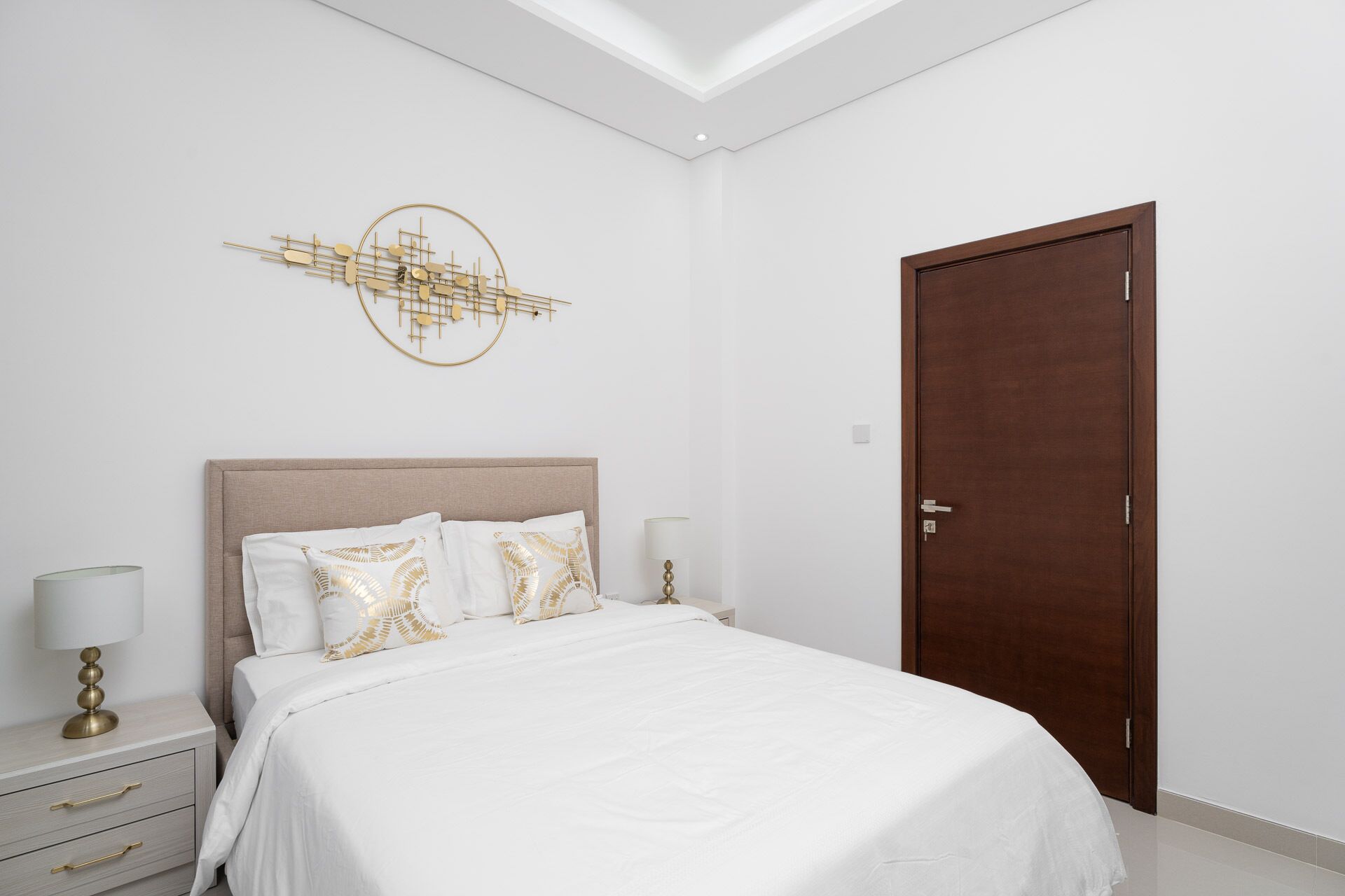 A bedroom with a bed, a nightstand, a lamp, a wall art piece, and a door.