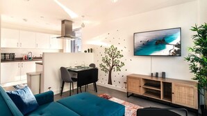 A modern living space with a teal sofa, a dining area, a kitchen, and a TV mounted on the wall. - Stunning Modern 1 Bed Apartment, Manchester (Salford)