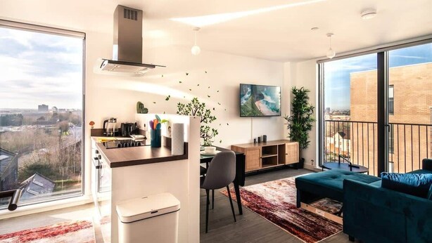 A modern apartment with a kitchen, dining area, and living room. It features large windows, a balcony, and a city view. - Stunning Modern 1 Bed Apartment, Manchester (Salford)