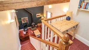 Un escalier avec une rampe en bois mène à un espace de vie comprenant une cheminée, des étagères et un canapé rouge.