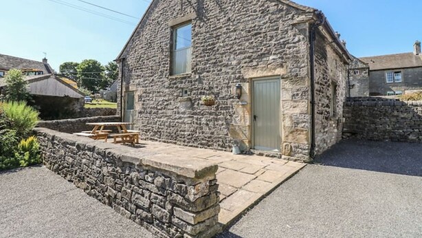 Une petite maison en pierre avec un petit porche et une table de pique-nique.