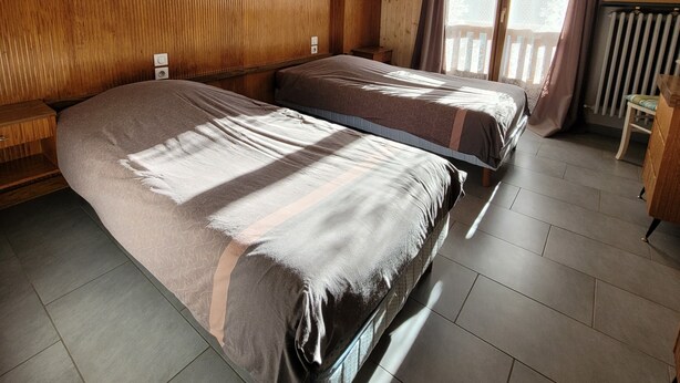Een kamer met houten lambrisering, twee bedden, een tafeltje en een raam met gordijnen.