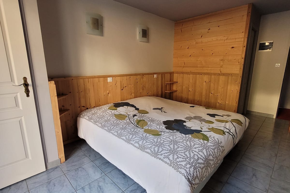 Un dormitorio con cama, cabecera de madera, suelo de baldosas y una puerta.