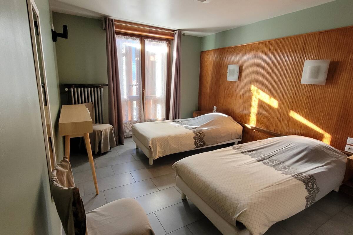 Habitación de hotel con dos camas, un radiador, una ventana con cortinas y un panel de pared de madera.