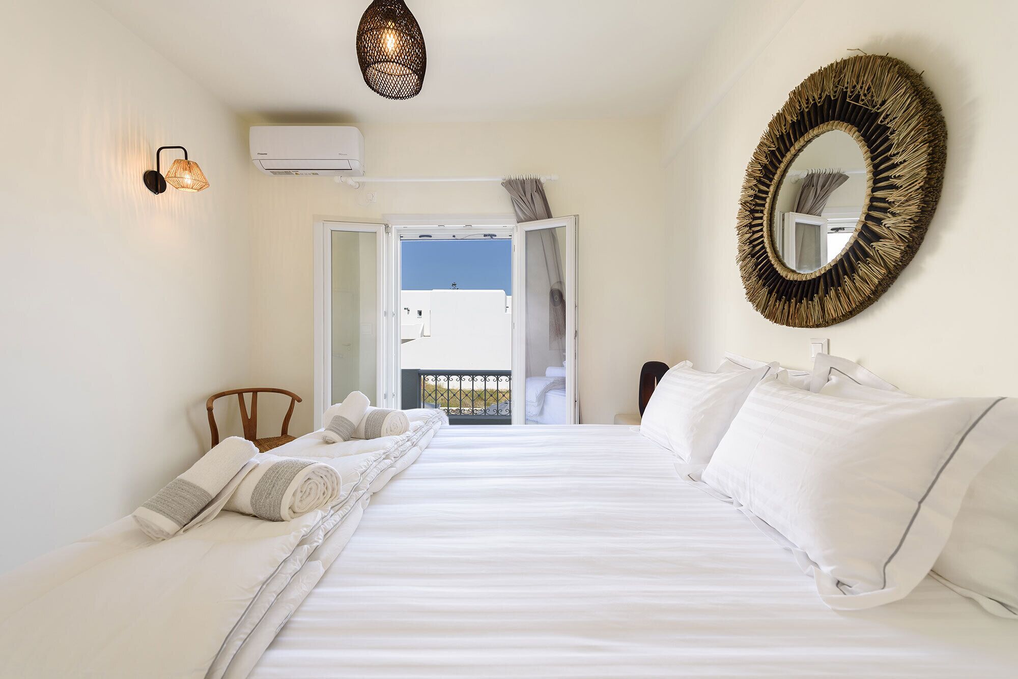 A hotel room with a large bed, a round mirror, and a view of the outside.