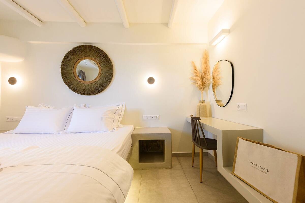 A bedroom with a bed, bedside table, desk, chair, and a mirror.