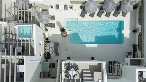 An aerial view of a modern hotel with a central swimming pool, multiple lounge areas with umbrellas, and a clean, white architectural design. - Vammos Luxury Apartments (Paros)