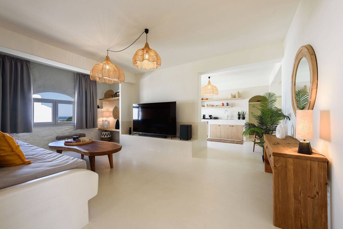 A modern living room with a sofa, coffee table, TV, and kitchen area with a dining table and chairs.