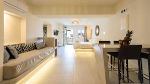 A modern hotel room with a sofa, a bed, a dining area, and a TV. - Vammos Luxury Apartments (Paros)