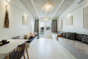 Una sala de estar moderna con un sofá, una mesa de comedor y un banco. Hay cortinas, una lámpara colgante y vistas al exterior.
