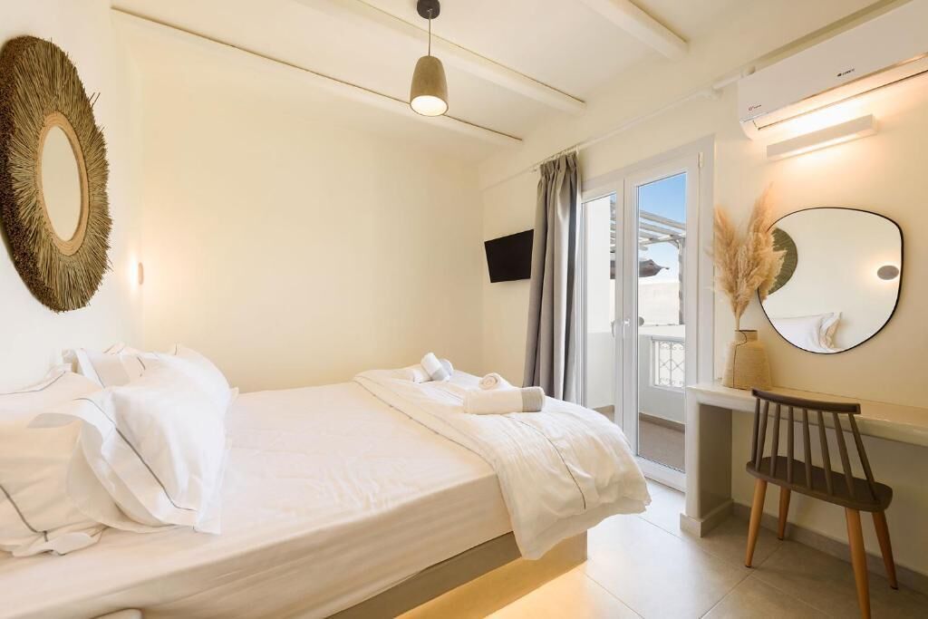 A hotel room with a bed, a desk, a chair, a round mirror, and a television.