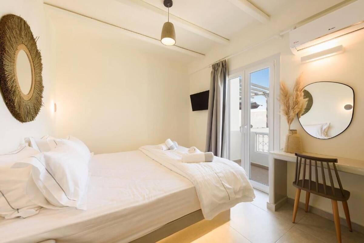 A hotel room with a bed, a desk, a chair, a round mirror, and a television.