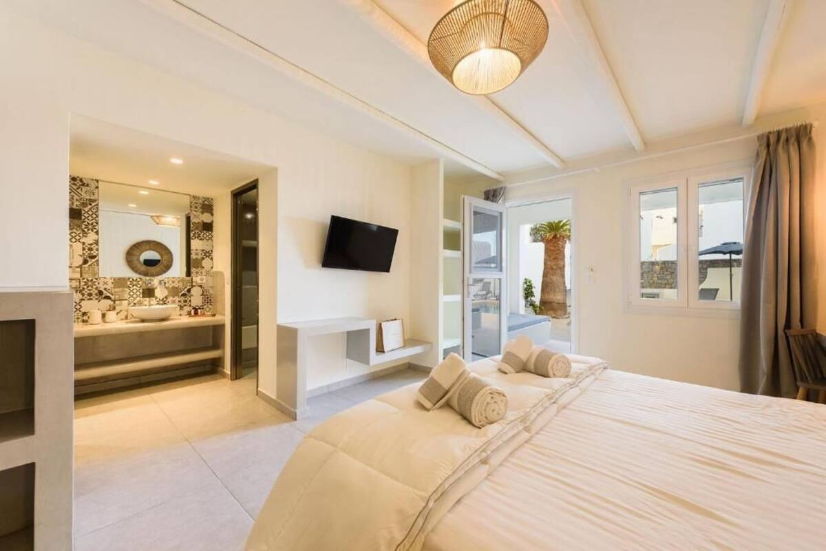 A bedroom with a bed, a TV, a bathroom with a sink, and a view of the outside.