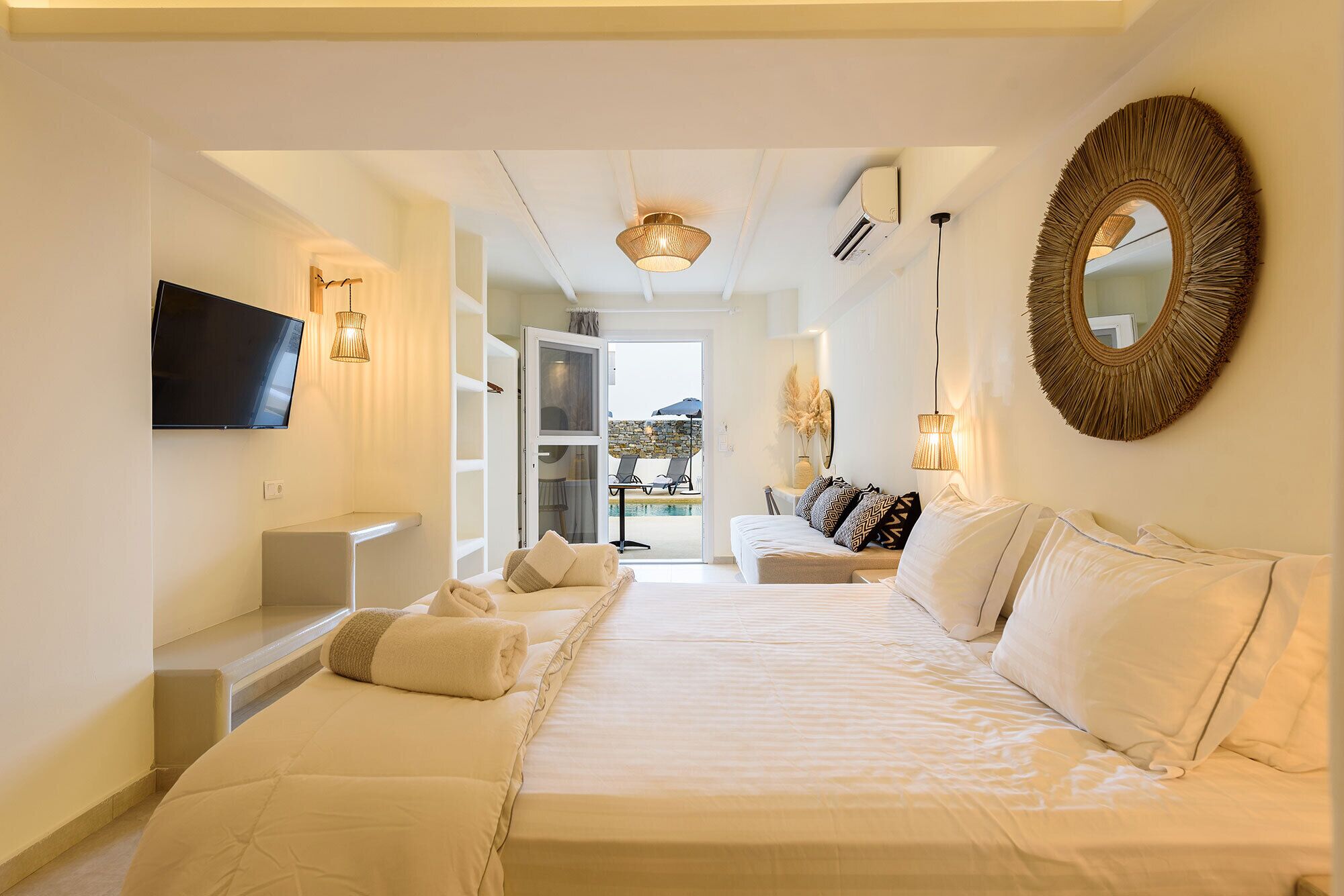 A hotel room with a large bed, a TV mounted on the wall, and a view of the pool area.